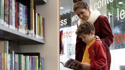 Motherandsonstandinginalibrarylookingatabooktogether