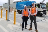 Two people wearing high visibility clothing and protective helmets standing in front of blue waste truck with Cleanaway logo.