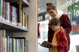 Motherandsonstandinginalibrarylookingatabooktogether