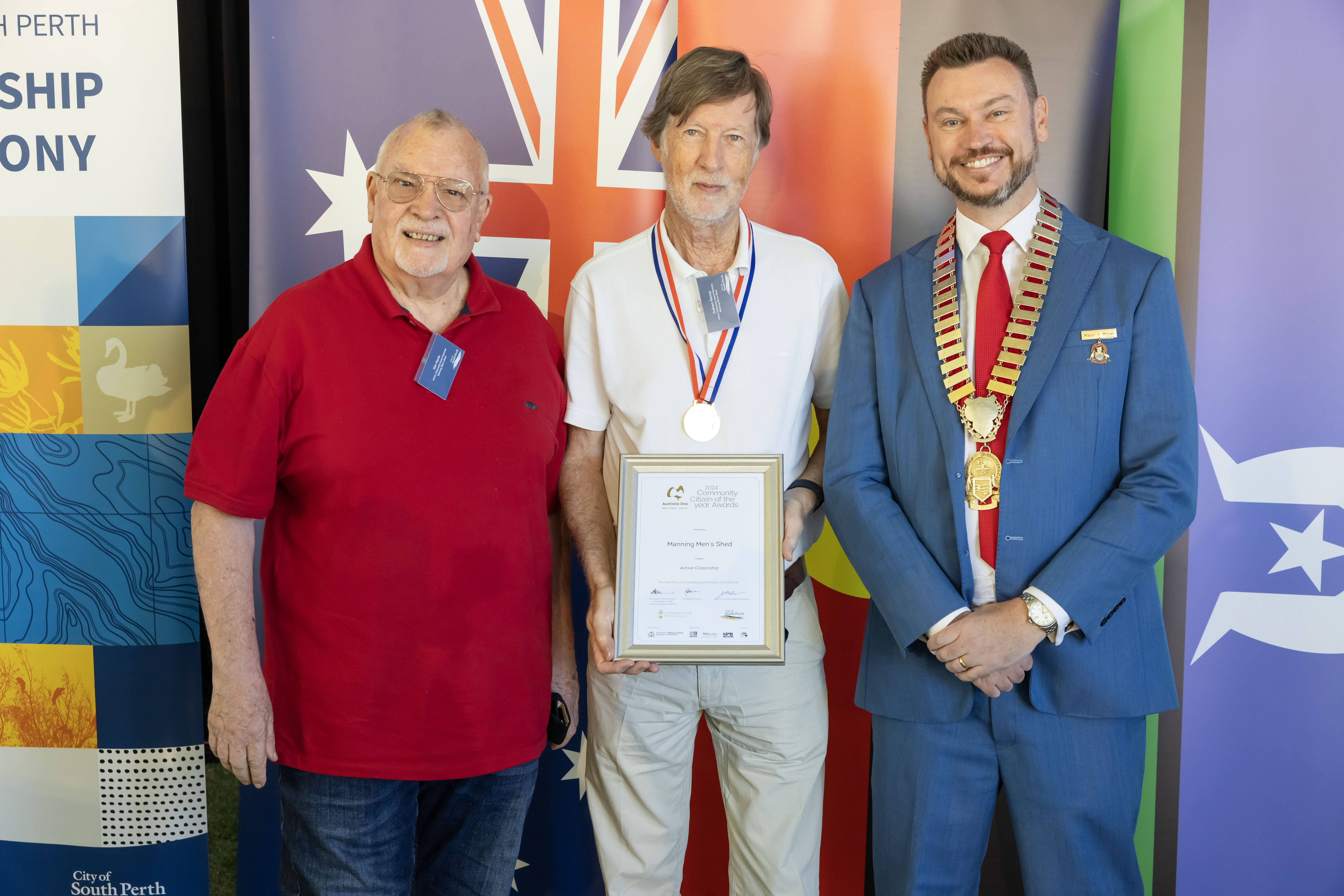 Three men smiling at the camera while one holds a framed certificate.