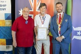 Three men smiling at the camera while one holds a framed certificate.