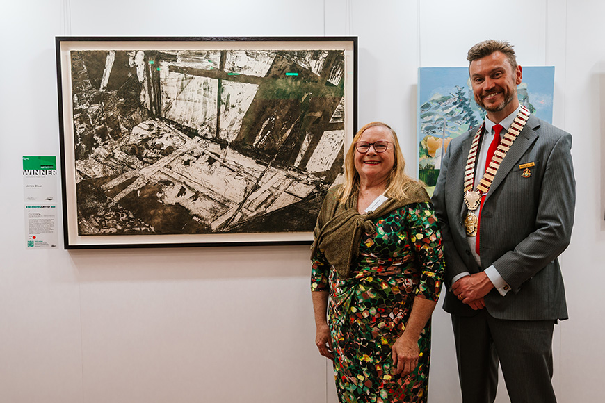 Two people standing proudly in front of an artwork.