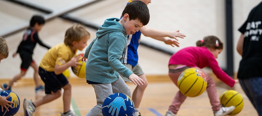 Agroupofsmallchildrenbouncingbasketballsonanindoorcourt