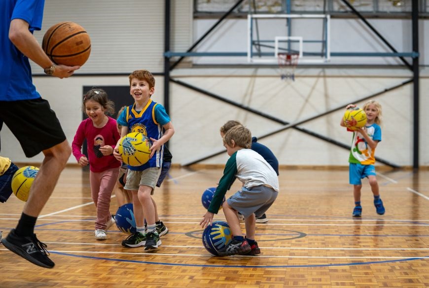 a group of children playing basketball with a coach at george burnett leisure centre