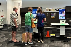 Three people standing in  front of self-service library kiosks