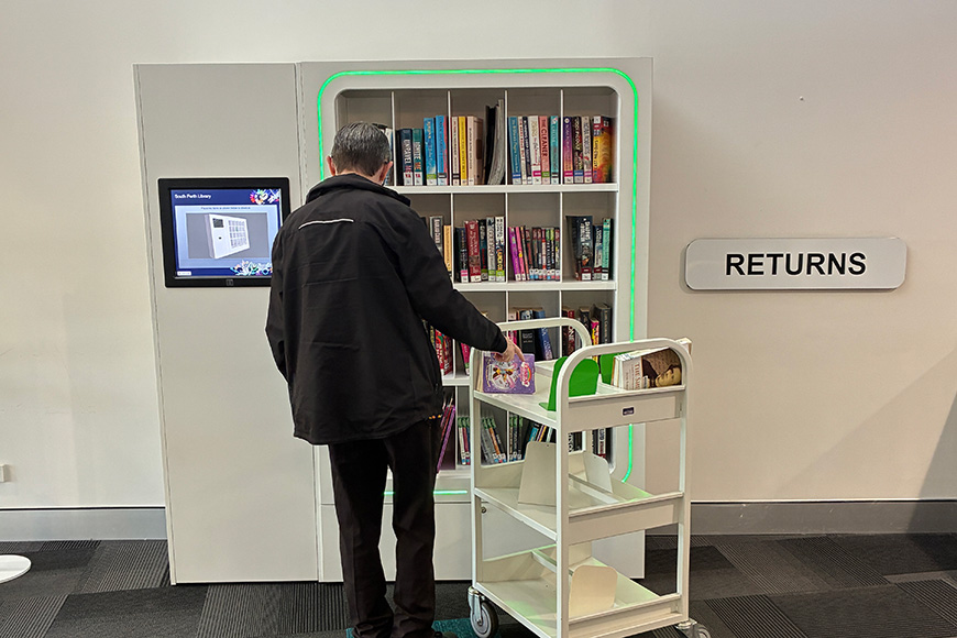 Someone standing with a book trolley in front of neon-lit book shelf.