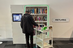 Someone standing with a book trolley in front of neon-lit book shelf.