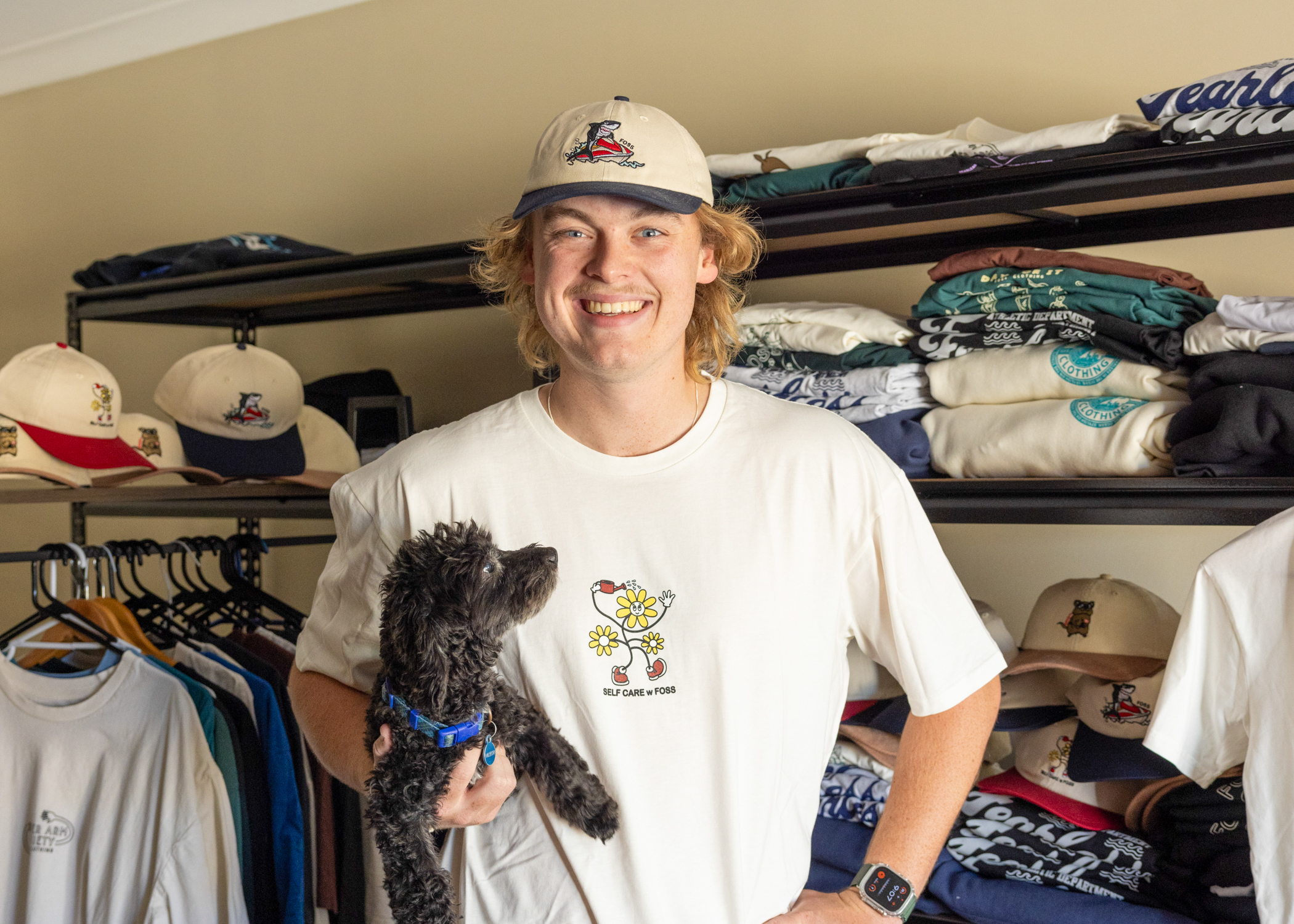 Person wearing a cap and a tshirt smiles at camera holding a brown dog