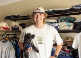 Person wearing a cap and a tshirt smiles at camera holding a brown dog