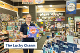 Person stands inside newsagency holding Shop Local sign