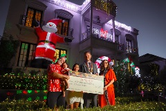 People smiling and holding a novelty cheque in front of a house covered in Christmas Lights