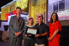 Four people smiling in front of a house covered in Christmas lights