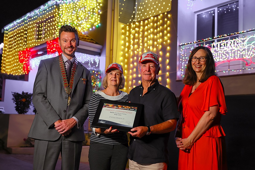 Four people smiling in front of a house covered in Christmas lights