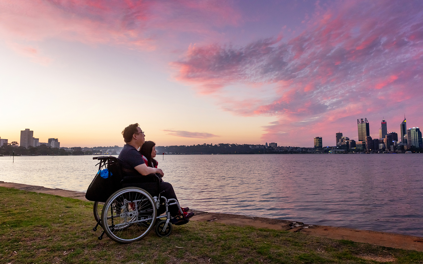 Person using wheelchair looking at river at dusk