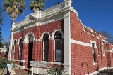 Diagonal view of the front of Heritage House showing red brick with cream features and large palm trees on a sunny day