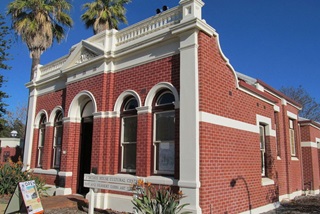 Diagonal view of the front of Heritage House showing red brick with cream features and large palm trees on a sunny day