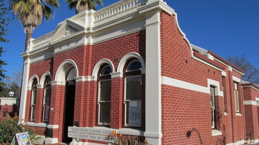 Diagonal view of the front of Heritage House showing red brick with cream features and large palm trees on a sunny day