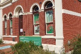 Diagonal view of the front of Heritage House showing red brick with cream features and large palm trees on a sunny day