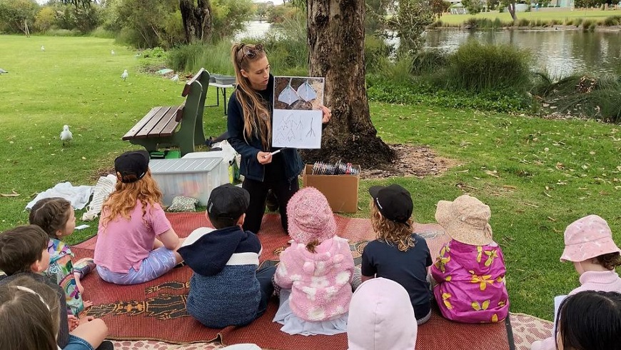 groupofchildrenlistentoawomanreadingabookoutdoors