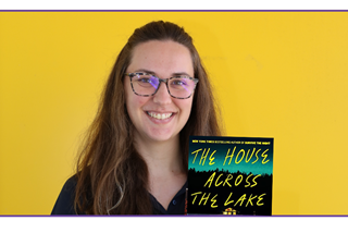 Librarianholdingabooktocamerainfrontofayellowwall
