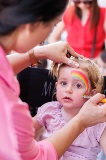 A young child getting a rainbow painted on their face.