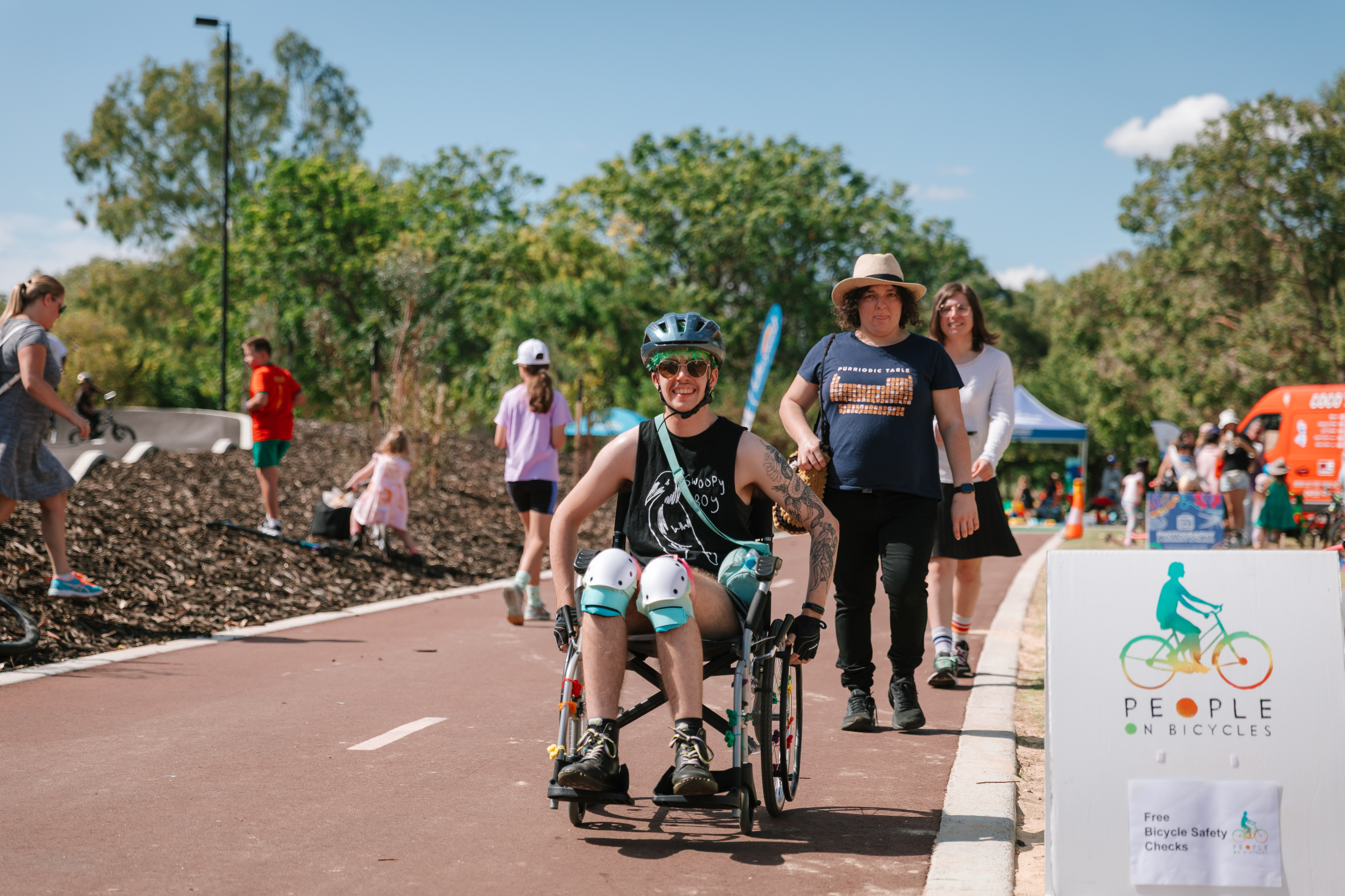 Man using wheelchair on bike track, with pedestrians and children the background.