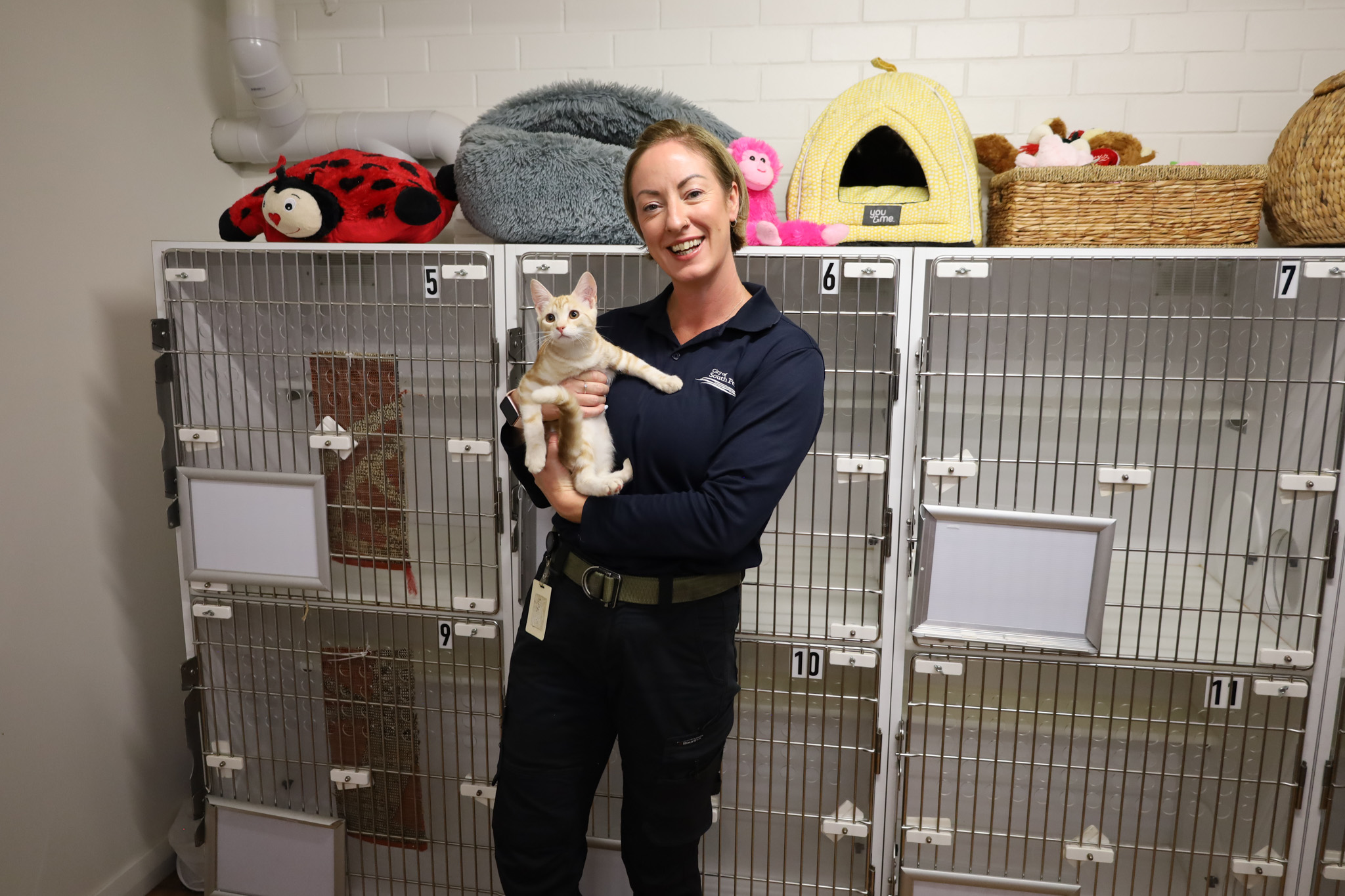 Staff holding cat in front of cat enclosure