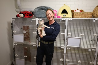 Staff holding cat in front of cat enclosure