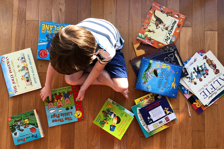 An aerial view of a child sitting on the ground surrounded by colourful books.