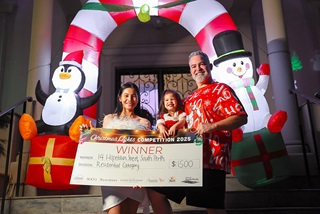 ThreepeopleholdinganoveltychequesmilinginfrontofacolourfulChristmasarch