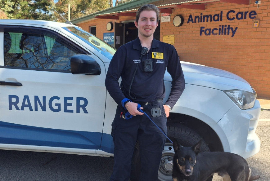 Ranger equipped with body camera standing in front of ranger vehicle with a dog on lead.