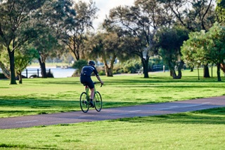 Manridinghisbikethroughaparkwithtreesandariveronacyclepath