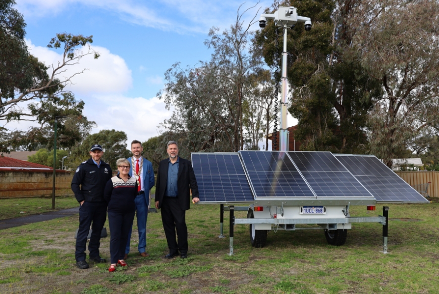 Police officer, Mayor, Local MP, and City staff member standing in front of a mobile CCTV trailer deployed at a park.