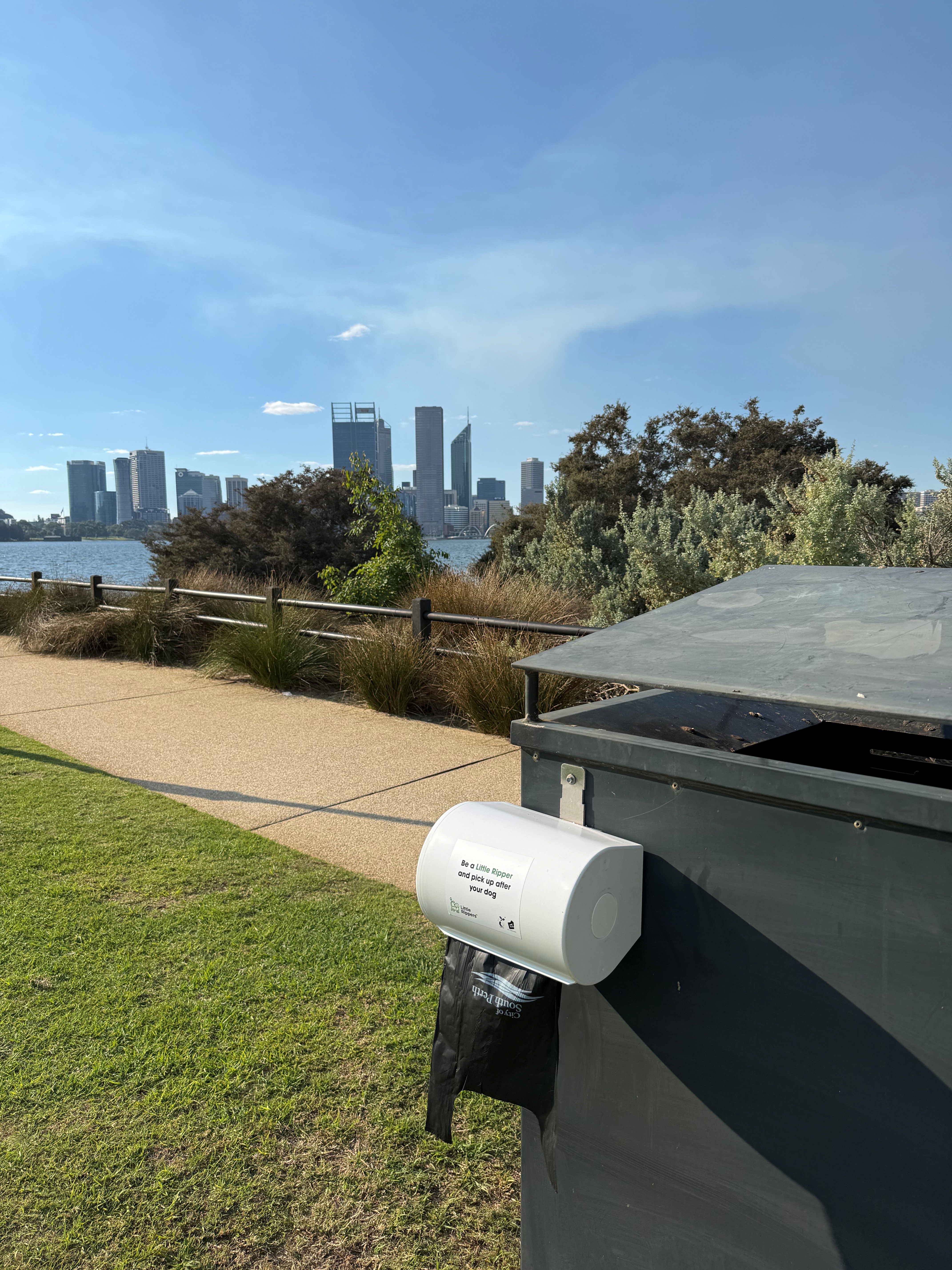 dog bag dispenser attached to bin in park next to footpath.