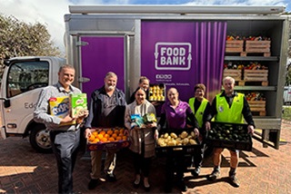 Agroupofpeopleinfrontofapurpletrucksmilingatcameraandholdingbasketsoffood