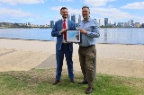 Twomenstandinginfrontoftheriverandholdingaframedgrantcertificate