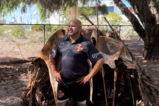 ManinfrontoftraditionalAboriginalhutwithkangarooskins