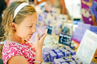 Younggirlsmellingahandmadebarofsoapatamarketstall