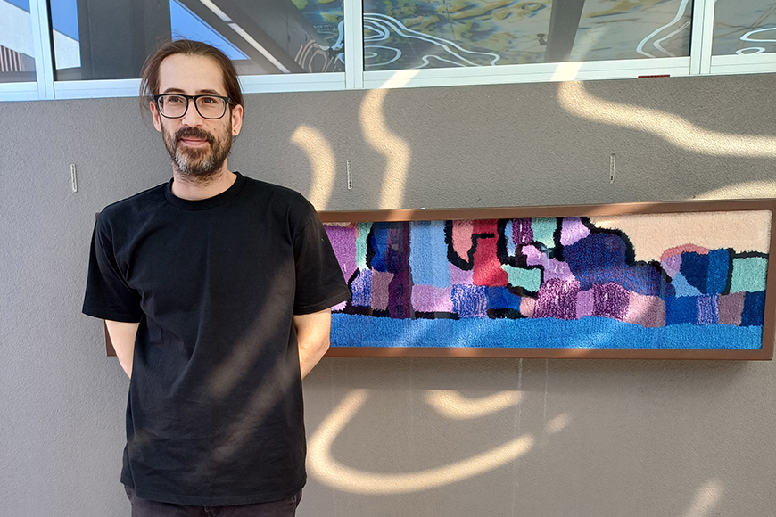 Someone smiling at camera in front of colourful artwork.