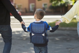 Ayoungchildwithaschoolbackpackholdinghandswithoneparenteachside