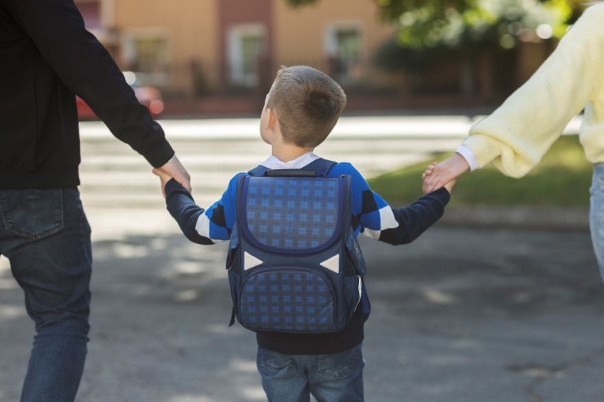 Ayoungchildwithaschoolbackpackholdinghandswithoneparenteachside
