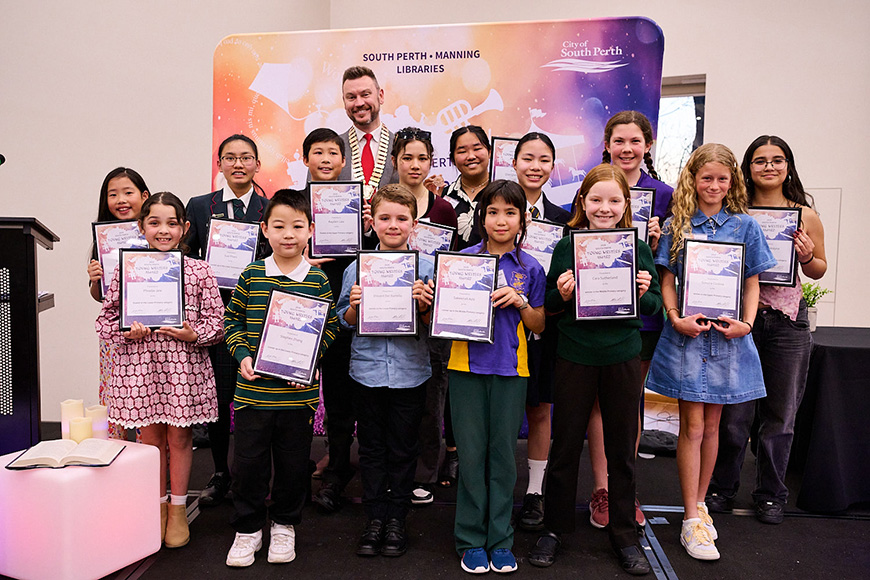 A group of children and a man standing in a group holding their awards