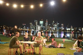 PeoplesittingatatableonthelawnalongtheriverwithCityskylinebackdrop