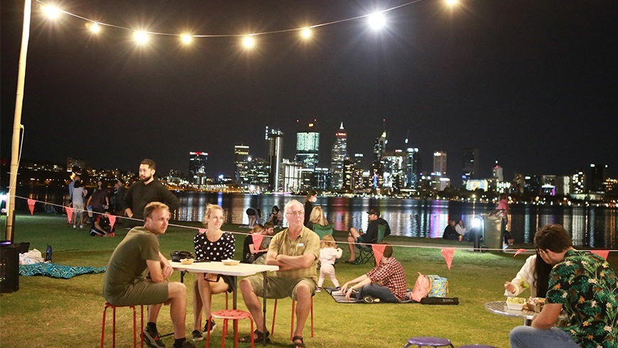 PeoplesittingatatableonthelawnalongtheriverwithCityskylinebackdrop