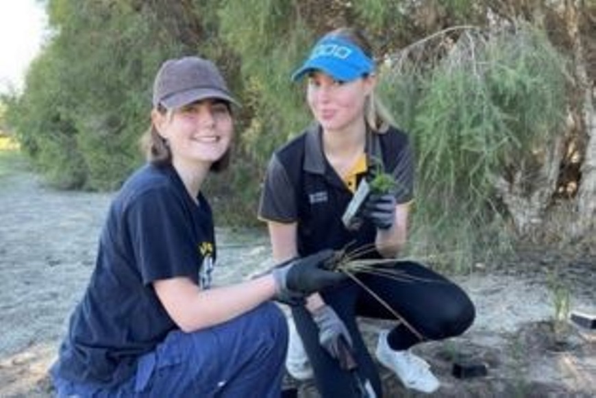 Twoyoungvolunteerskneelingandholdingseedlings