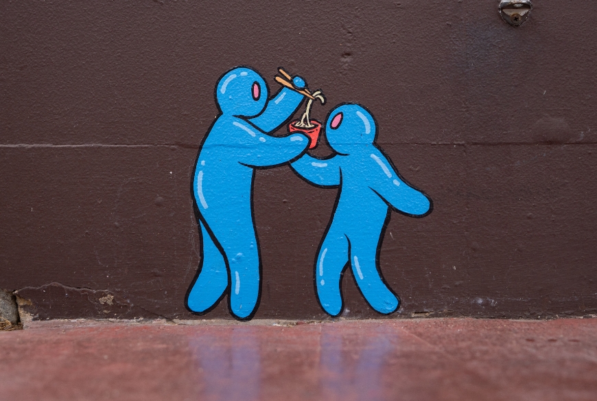 A wall mural with two blue characters sharing noodles from a single bowl.
