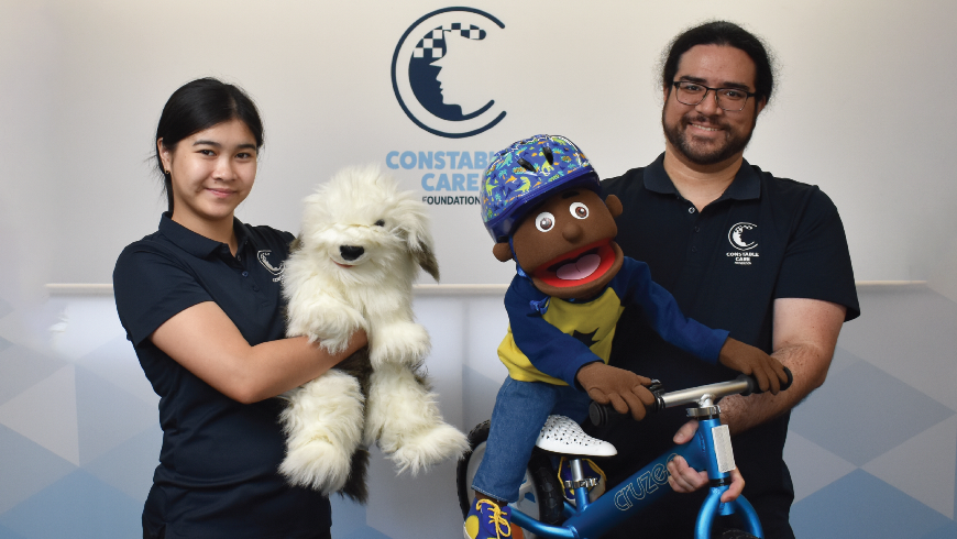 Twoconstablecareofficerstheofficerontherightisholdingapuppetofachildonabicycletheofficerontheleftisholdingadogpuppet